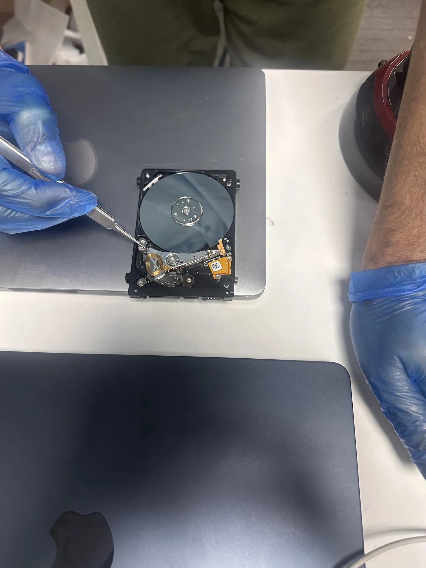 TechFix technician using tweezers on an opened hard drive platter during data recovery in Faisalabad