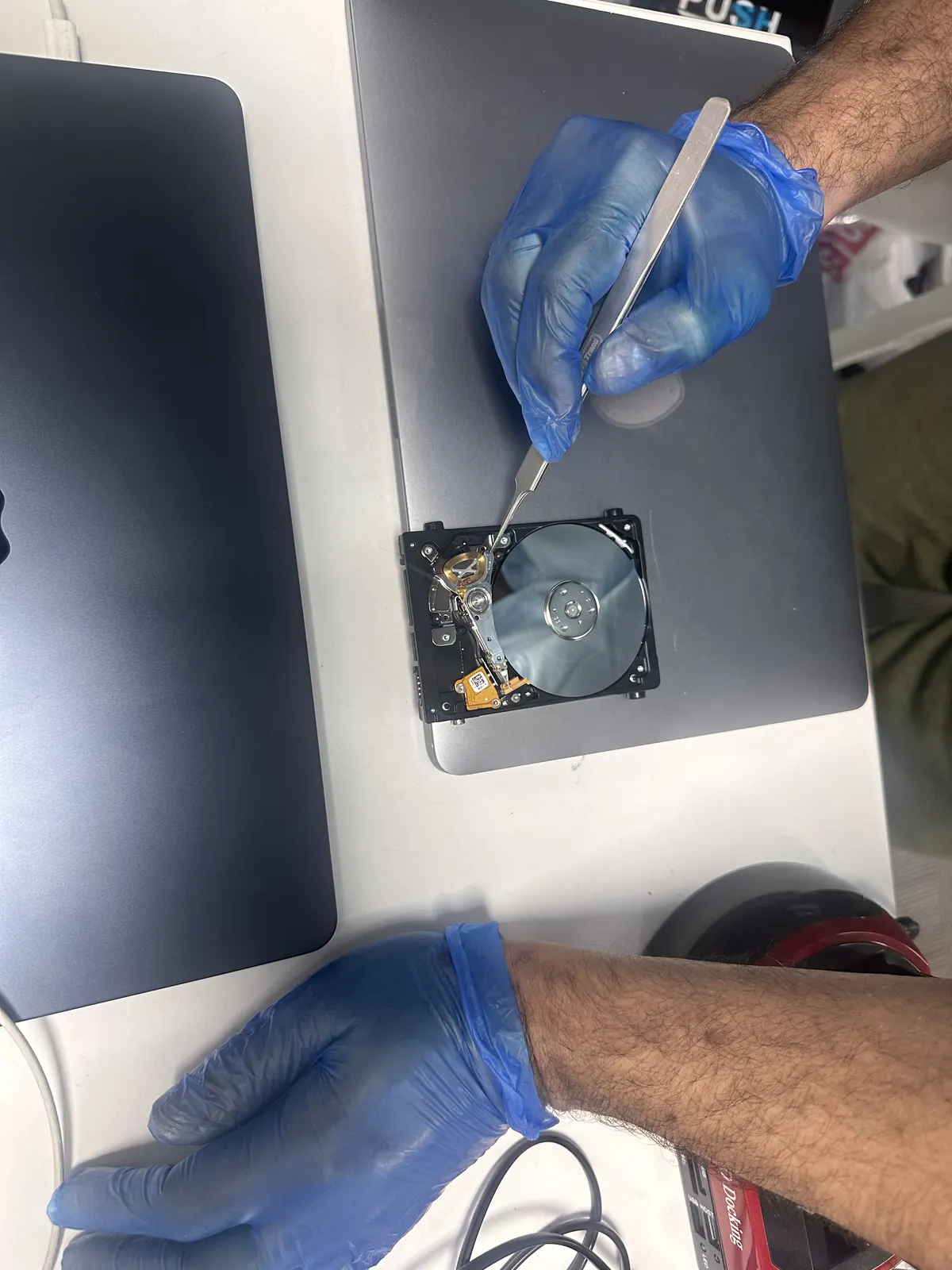 Technician using tweezers on an opened hard drive platter during data recovery