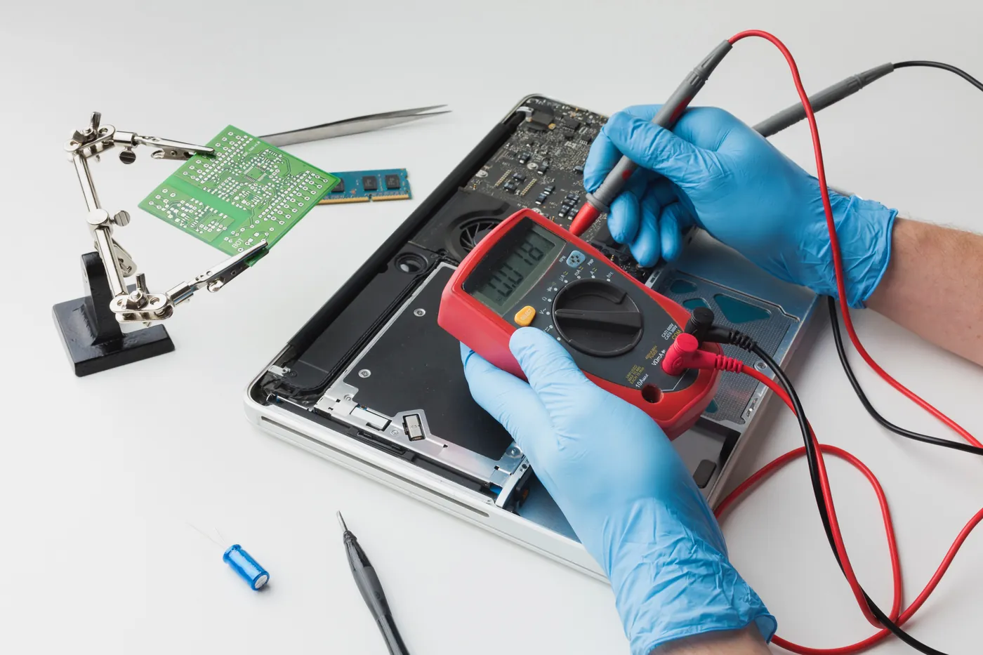 Gloved technician measuring voltage on a MacBook logic board