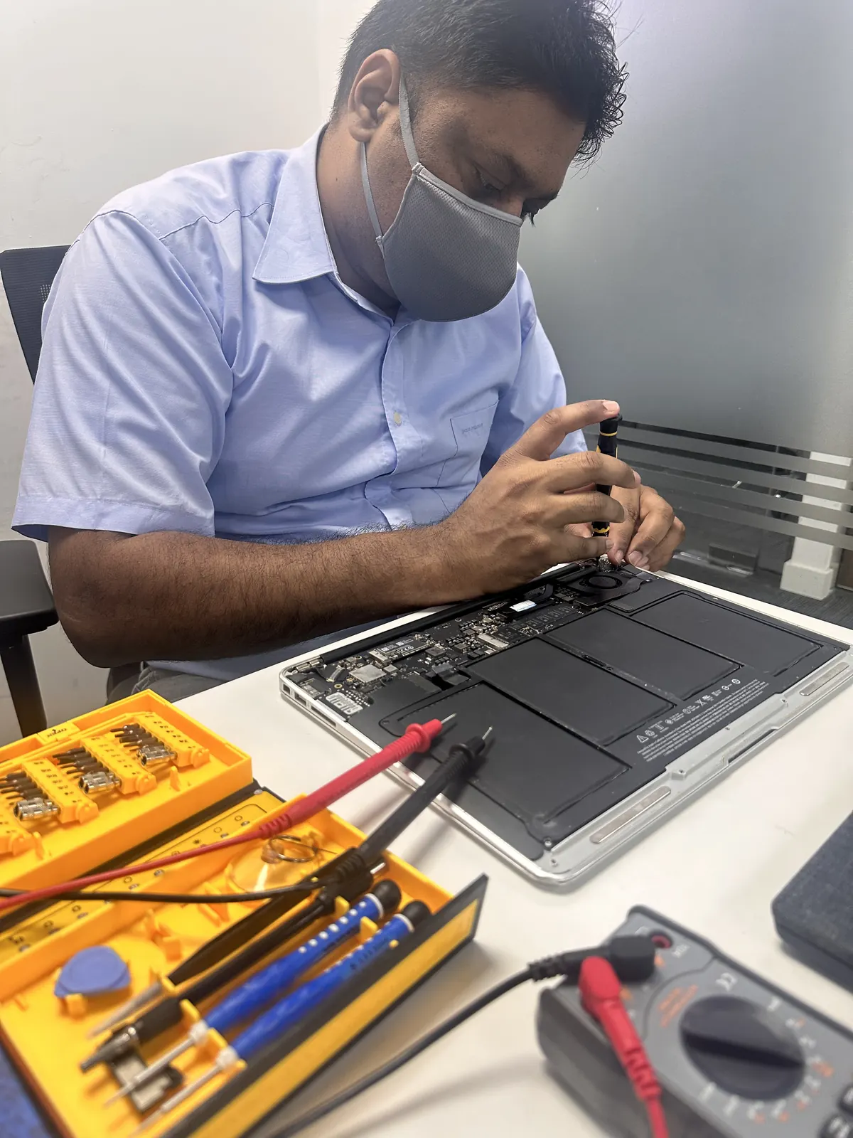 Technician testing a MacBook board with a multimeter